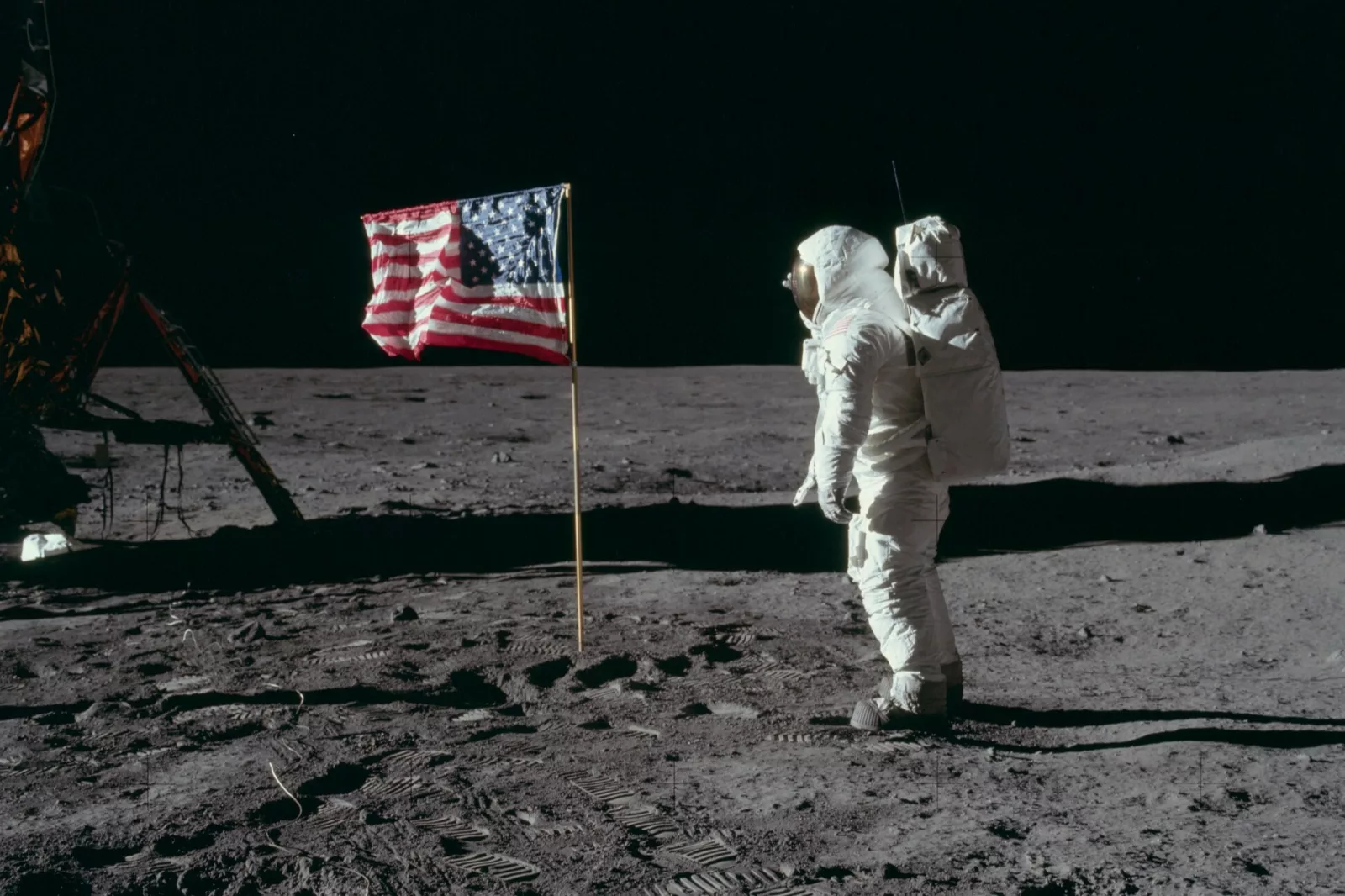 A photograph of an astronaut on the moon facing an American flag.