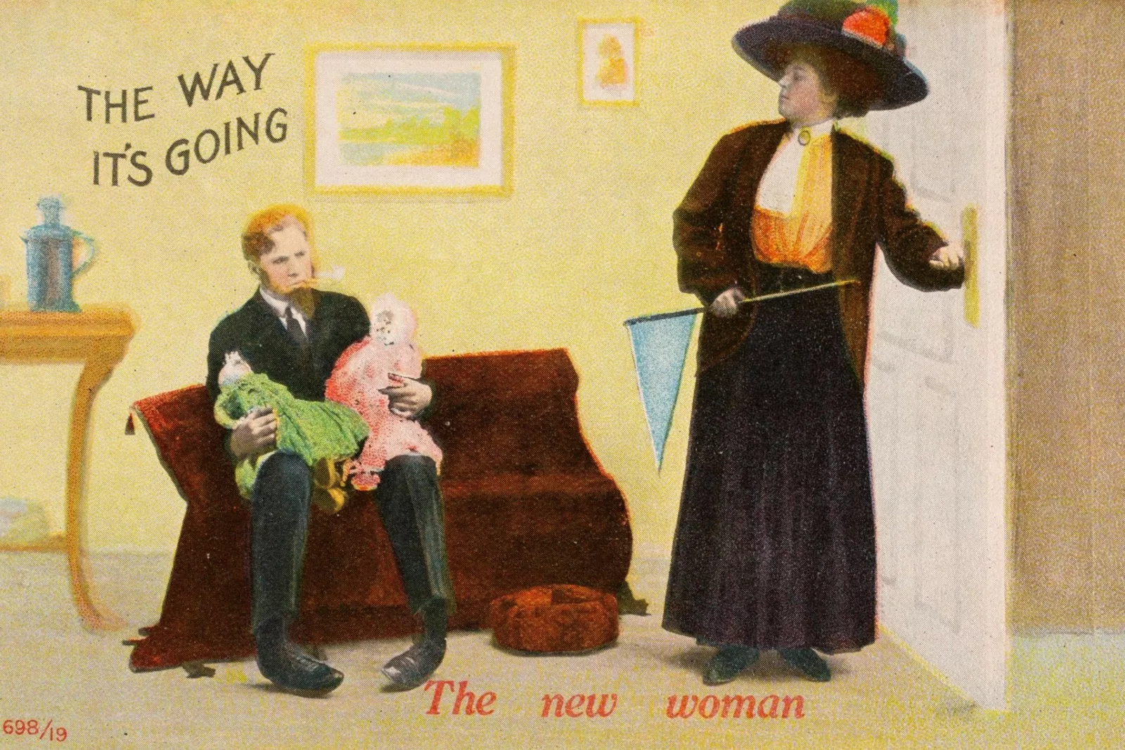 A postcard depicting a woman holding a pennant and heading out the door while a man sits on the couch and holds two babies. Text at the top reads, "The way it's going," and on the bottom, "The new woman."