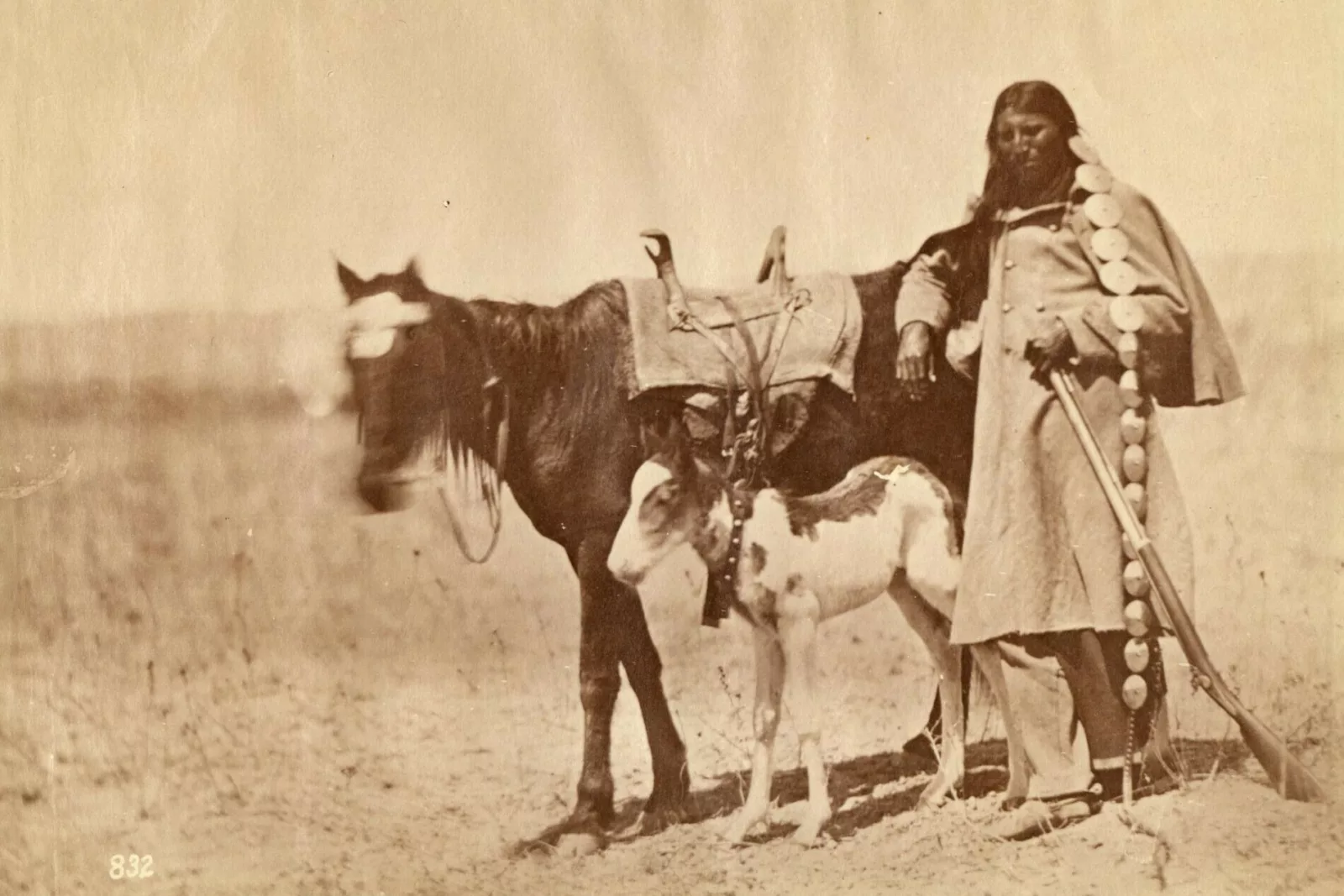 A sepia-toned photograph of a man, a horse, and a foal.